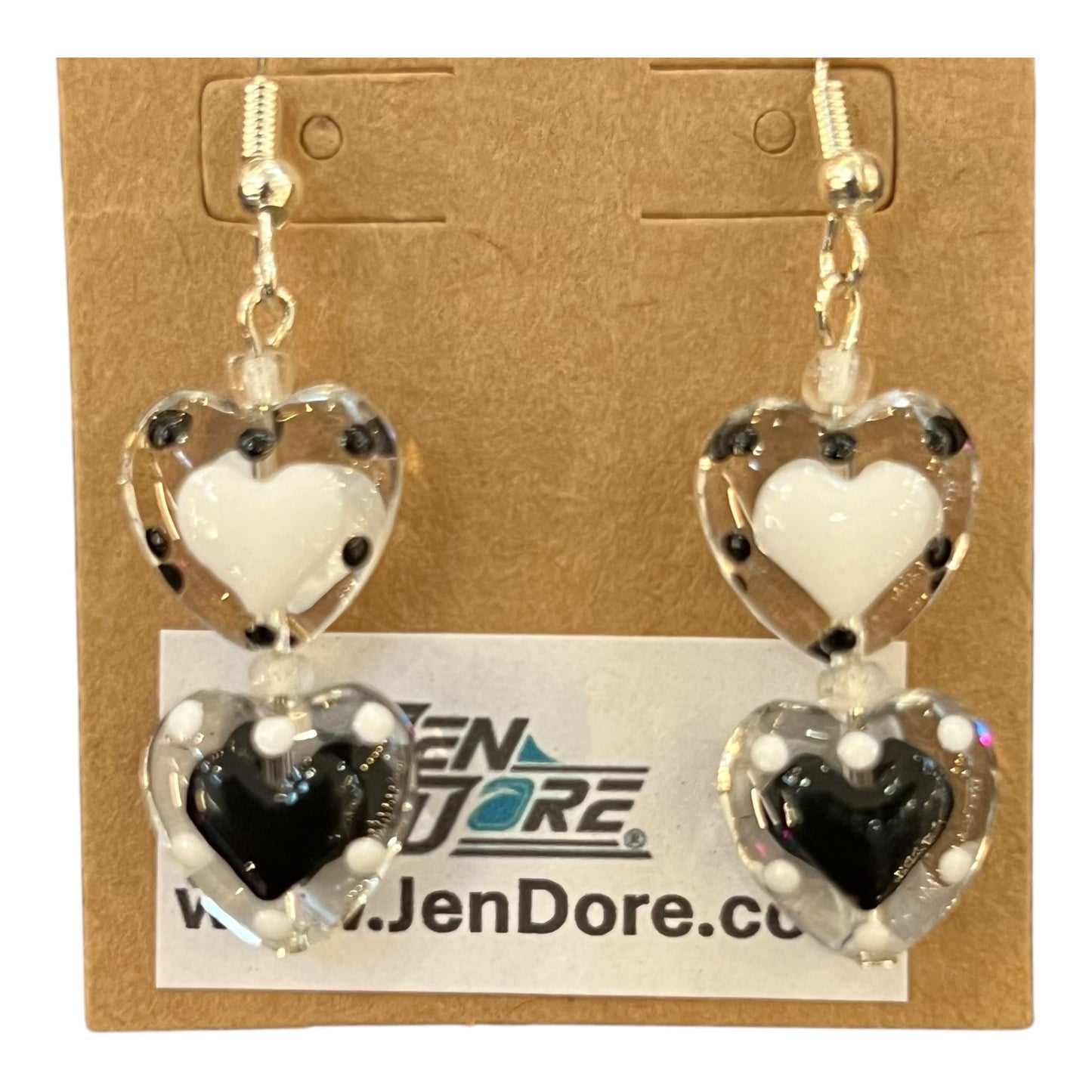 Heart-shaped earrings with white, black, and clear design on a JenDore card.
