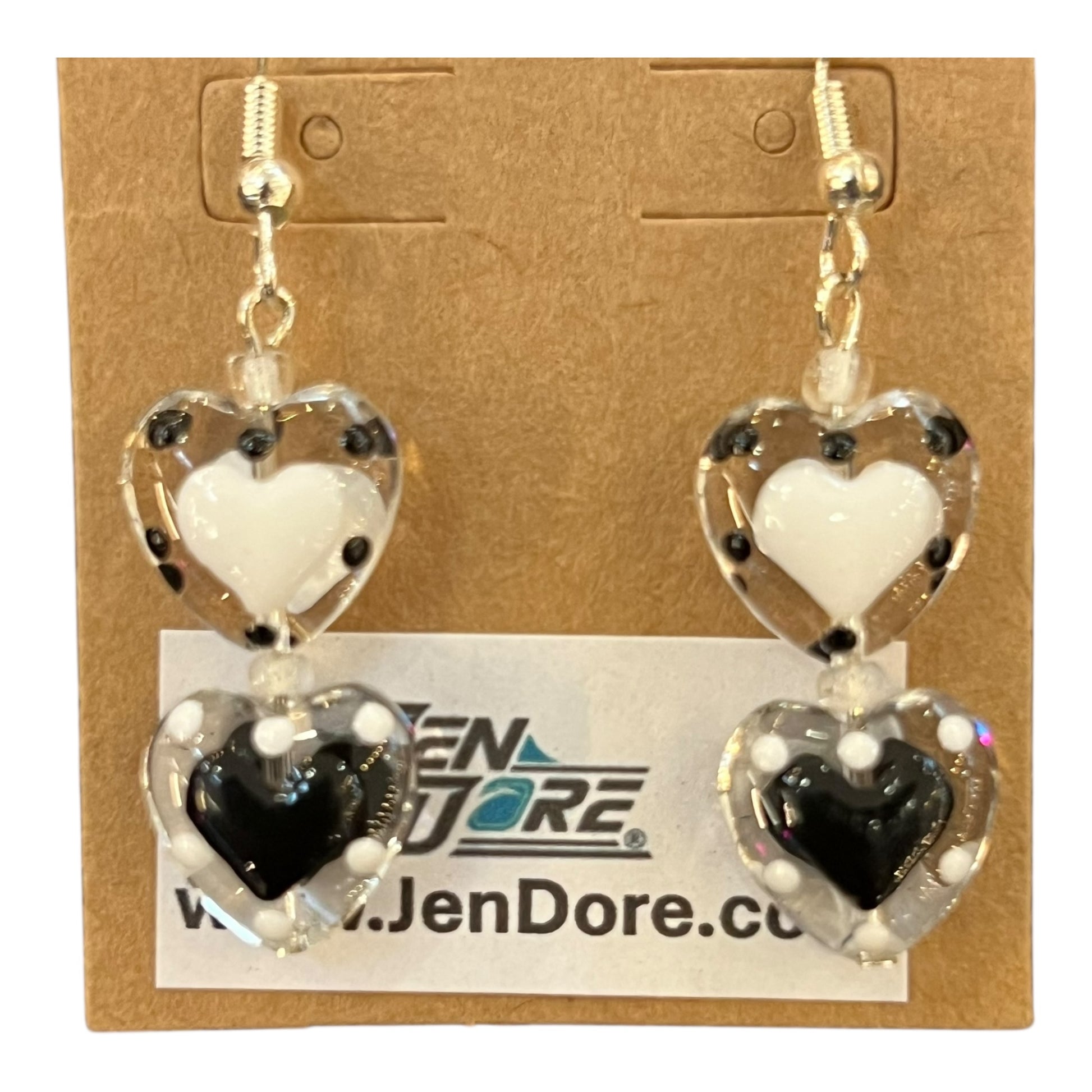 Heart-shaped earrings with white, black, and clear design on a JenDore card.
