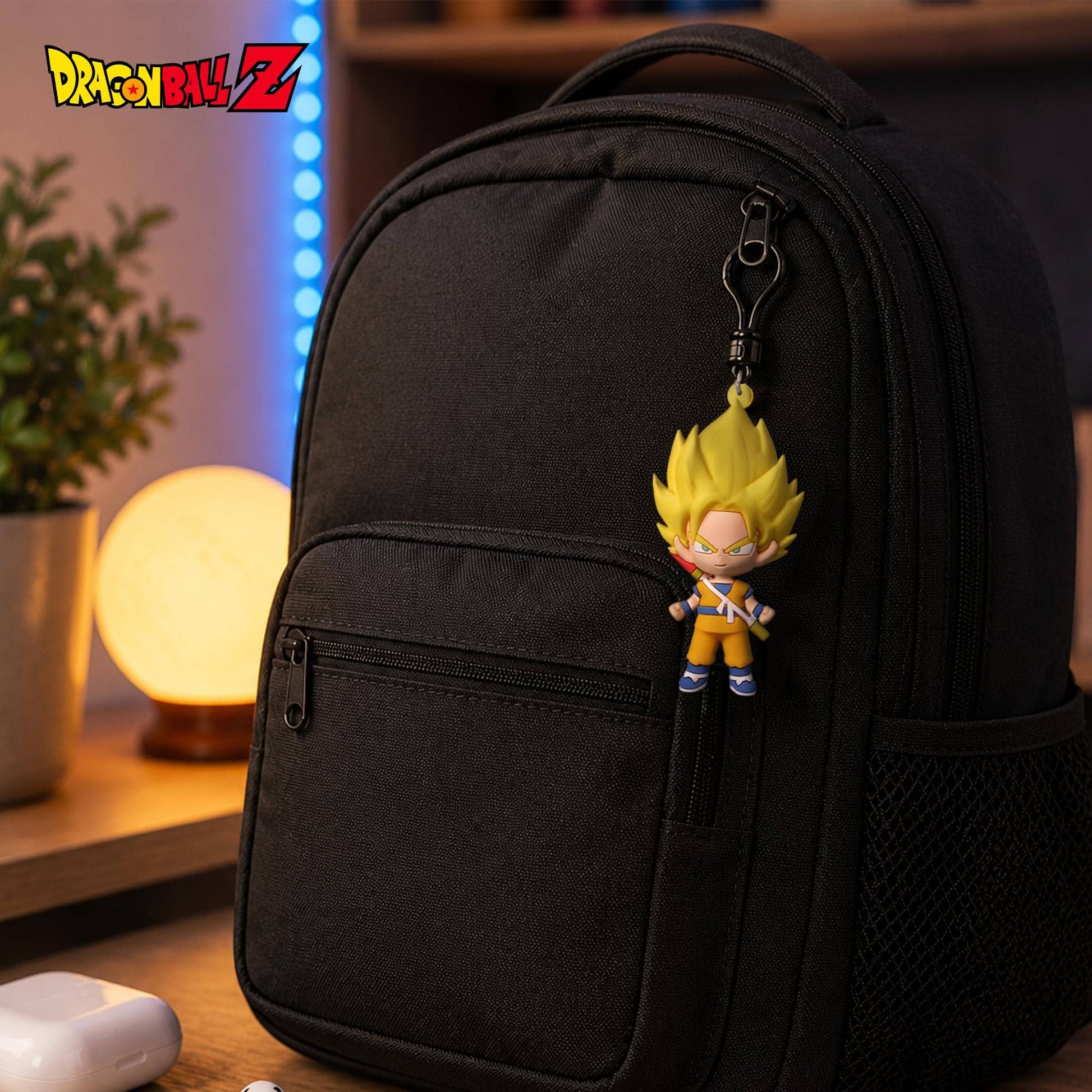 A black backpack with a Dragon Ball Z character charm hanging from the zipper, shown in a warm, dimly lit indoor setting with a glowing lamp and plant in the background.