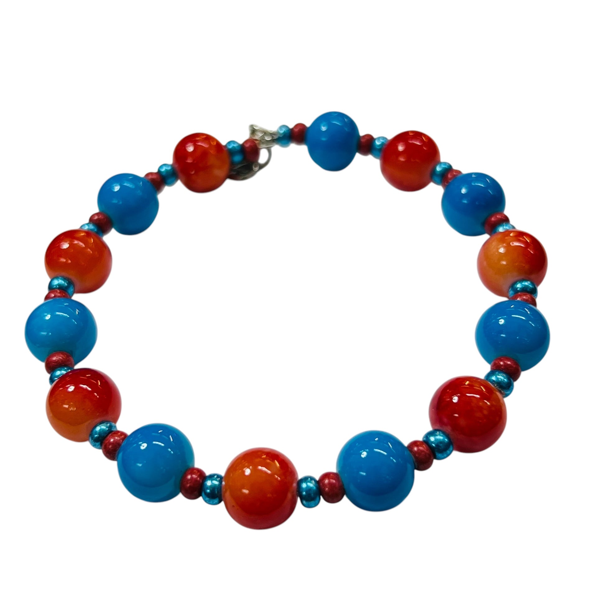 A beaded necklace featuring alternating large glossy blue and red-orange beads, with smaller metallic teal and red spacer beads, and a small silver clasp, shown on a plain white background.
