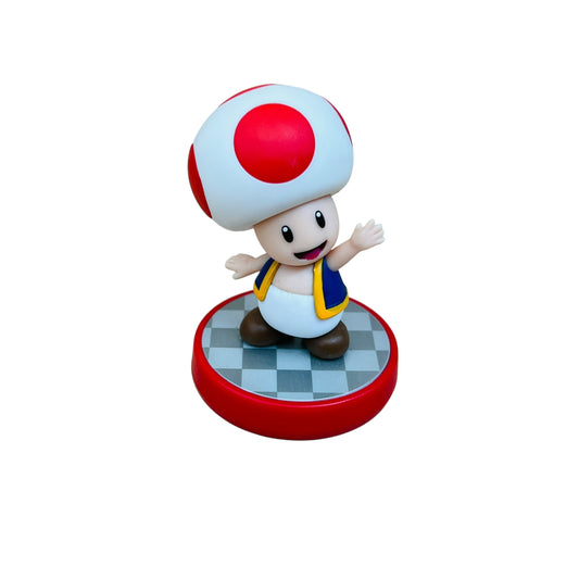 Toy figure of a character with a red and white mushroom cap on a checkered platform, on a white background.